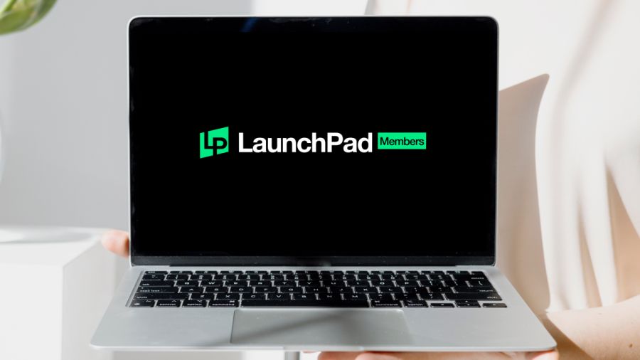 A person holds a silver laptop displaying the "LP LaunchPad Members" logo on its black screen.