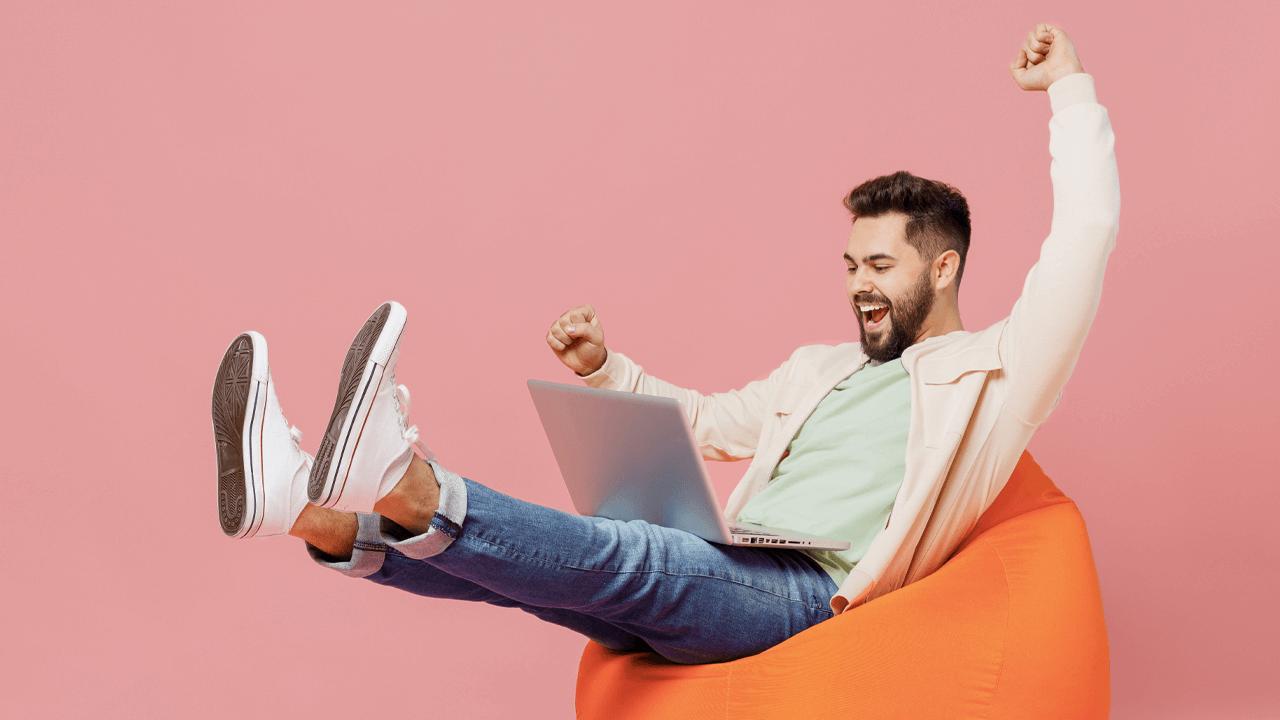 Excited man with laptop on a beanbag chair.