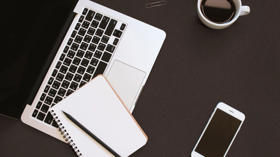 Workspace with a laptop, notebook, pencil, smartphone, and coffee cup on a dark surface.