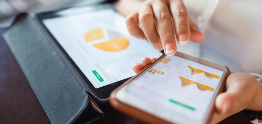 A person's hands interacting with a smartphone and tablet, both displaying charts.