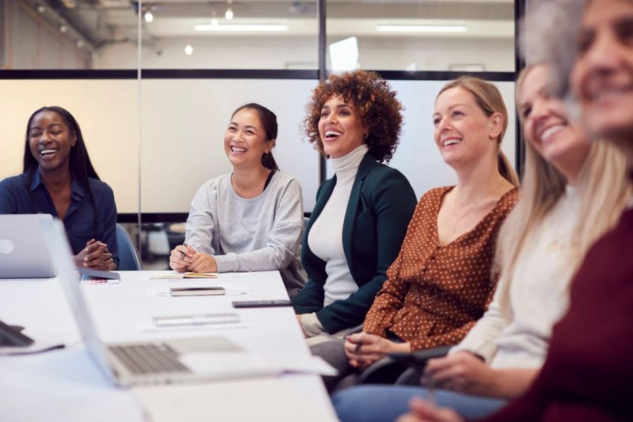 A diverse group of women smiling and laughing at a business meeting.