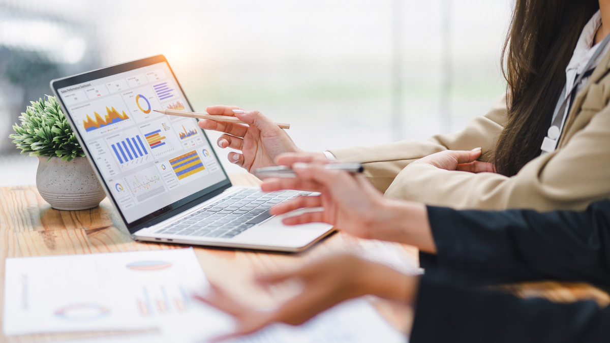 Two people discuss data charts on a laptop, one pointing at the screen.