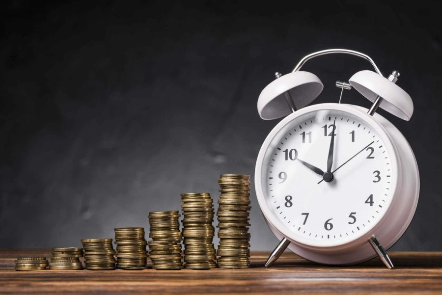 Progressively taller stacks of coins next to a white alarm clock.