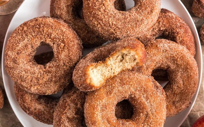 Cross section of a baked apple cider donut showing tender crumb with cinnamon sugar coating and apple cider reduction glaze on a dark wooden board
