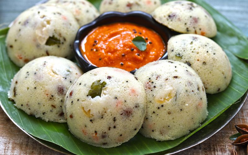 Idli batter in a large container showing fully fermented risen batter with bubbles ready for steaming in an idli steamer mould