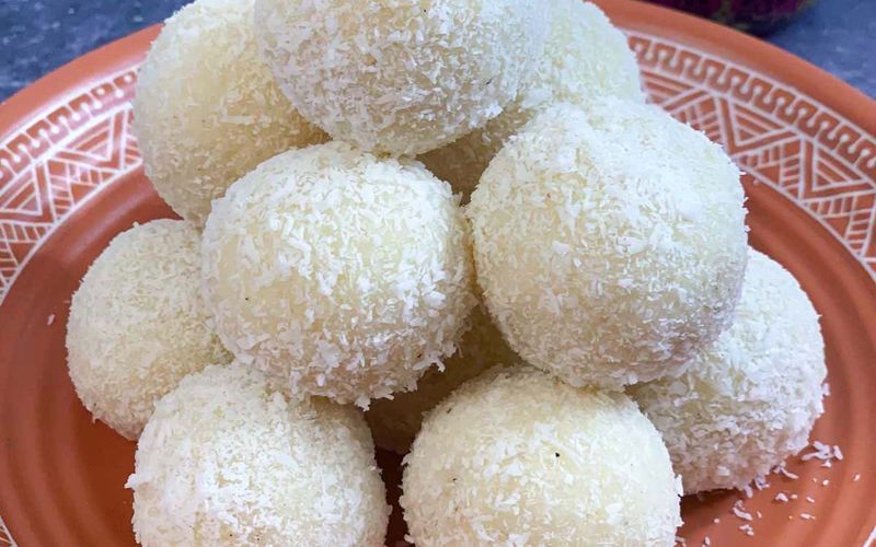 Three versions of homemade coconut ladoo recipe showing fresh coconut ladoo condensed milk ladoo and milk powder ladoo side by side on a wooden board