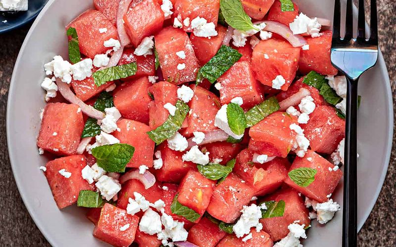 Mediterranean watermelon feta salad with cucumber red onion Kalamata olives fresh mint and extra virgin olive oil drizzle on a serving platter