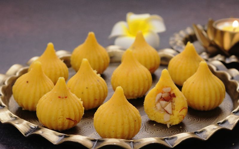 Step by step mawa modak recipe showing khoya cooking in a heavy pan and shaped modak garnished with saffron and pistachios for festival gifting
