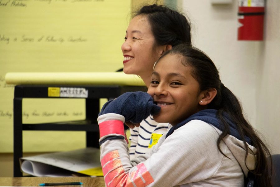A girl sits next to a mentor, smiling at the camera