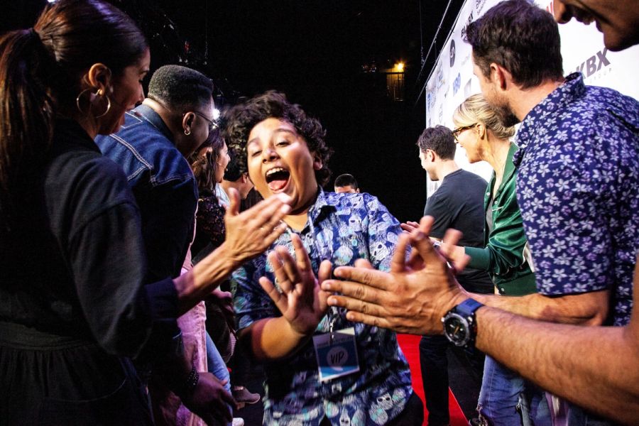 A student goes down a red carpet, high fiving actors