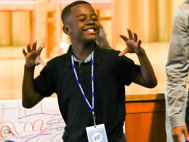 A boy holds his hands up, eyes closed, smiling