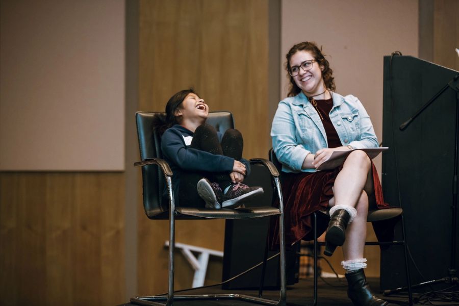 A mentor and student laugh next to each other on stage