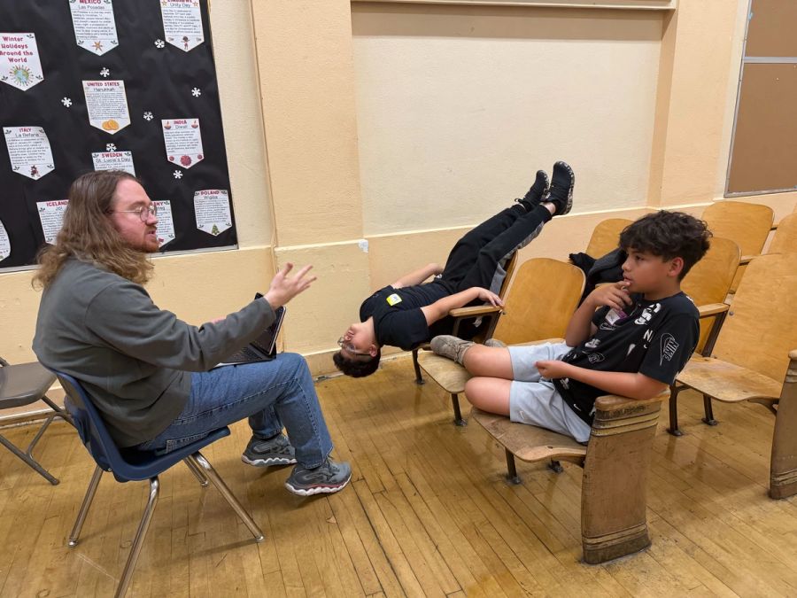 A man sits across from two boys, one seated upright and the other seated upside down