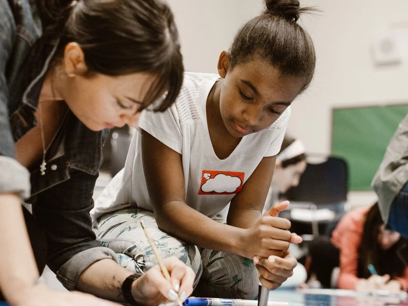 A girl and a woman work on a poster together on the ground