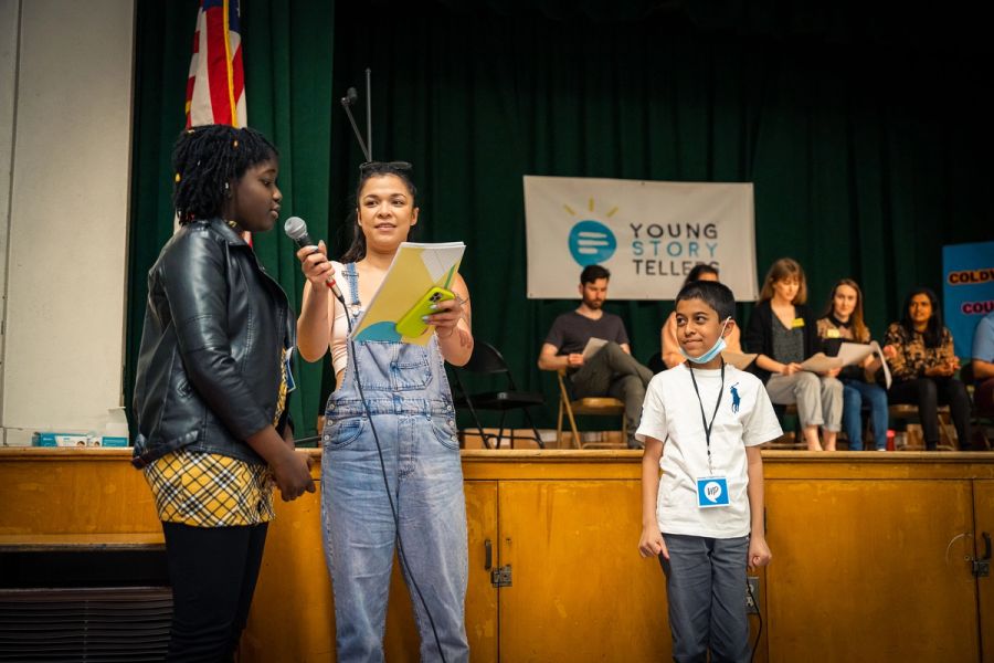 A mentor stands between a boy and girl, holding a mic up to the girl