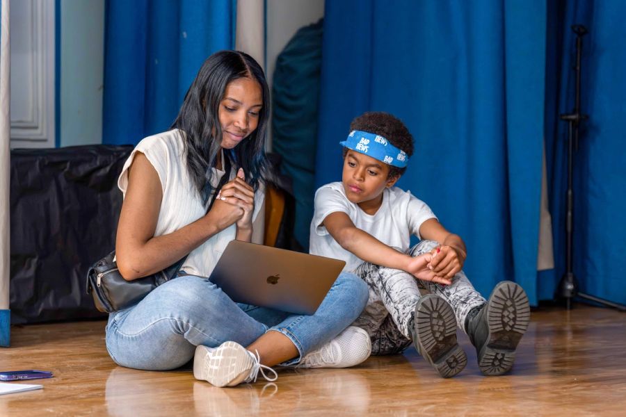 A woman and a boy sit next to each other on the floor, looking at a laptop