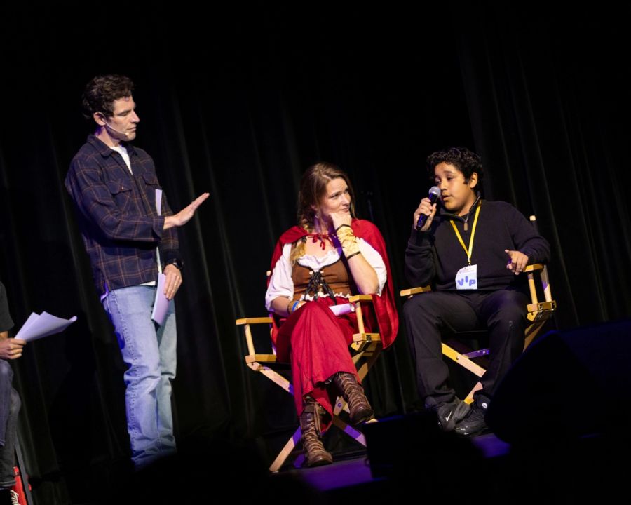 A student and a mentor sit in chairs, and a man stands next to them
