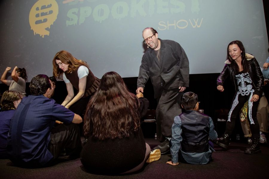 Students sit on a stage, actors in front of them smile and reach out their hands