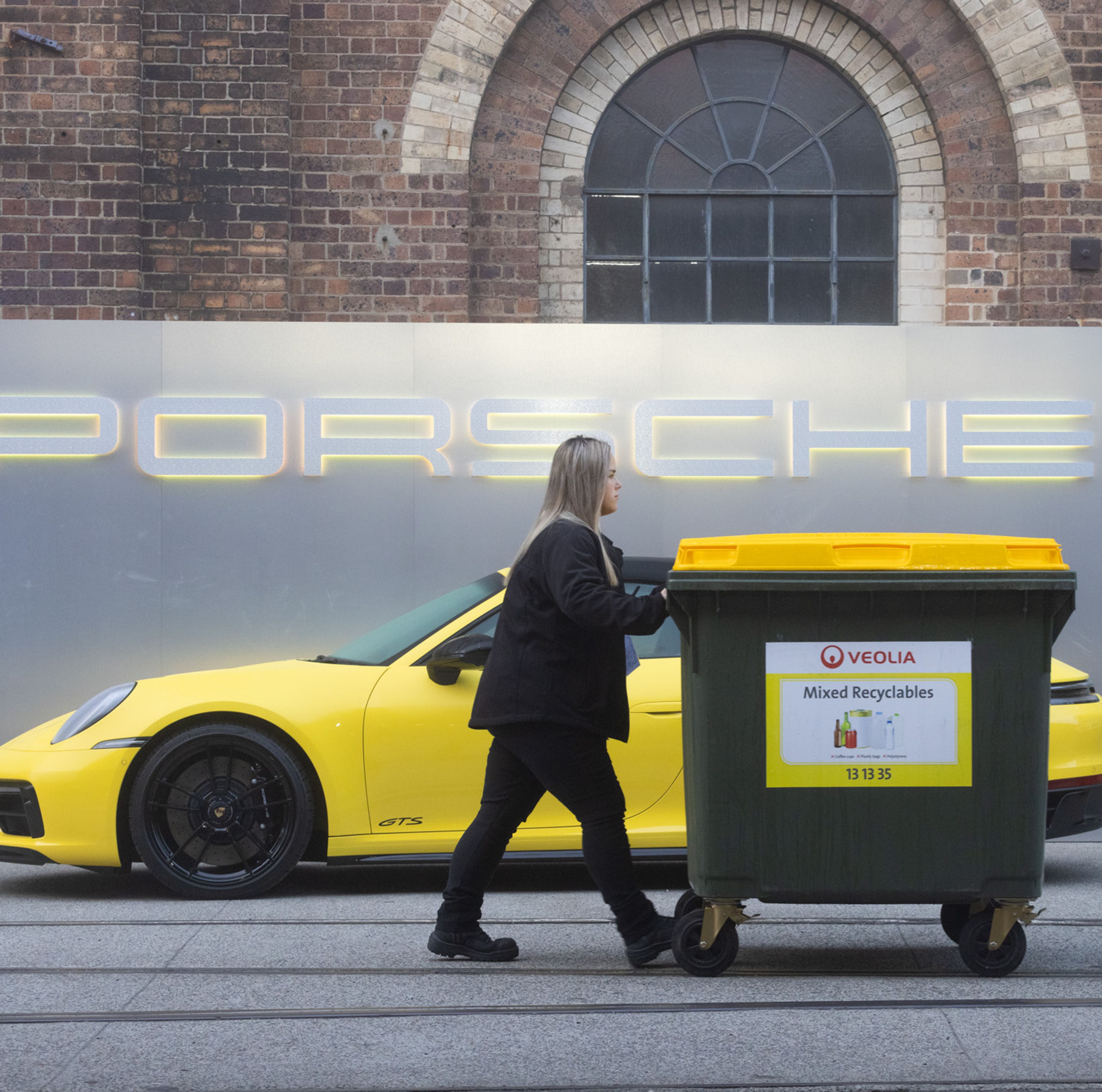 Clean Vibes staff wheeling a recycling bin in front of yellow porche