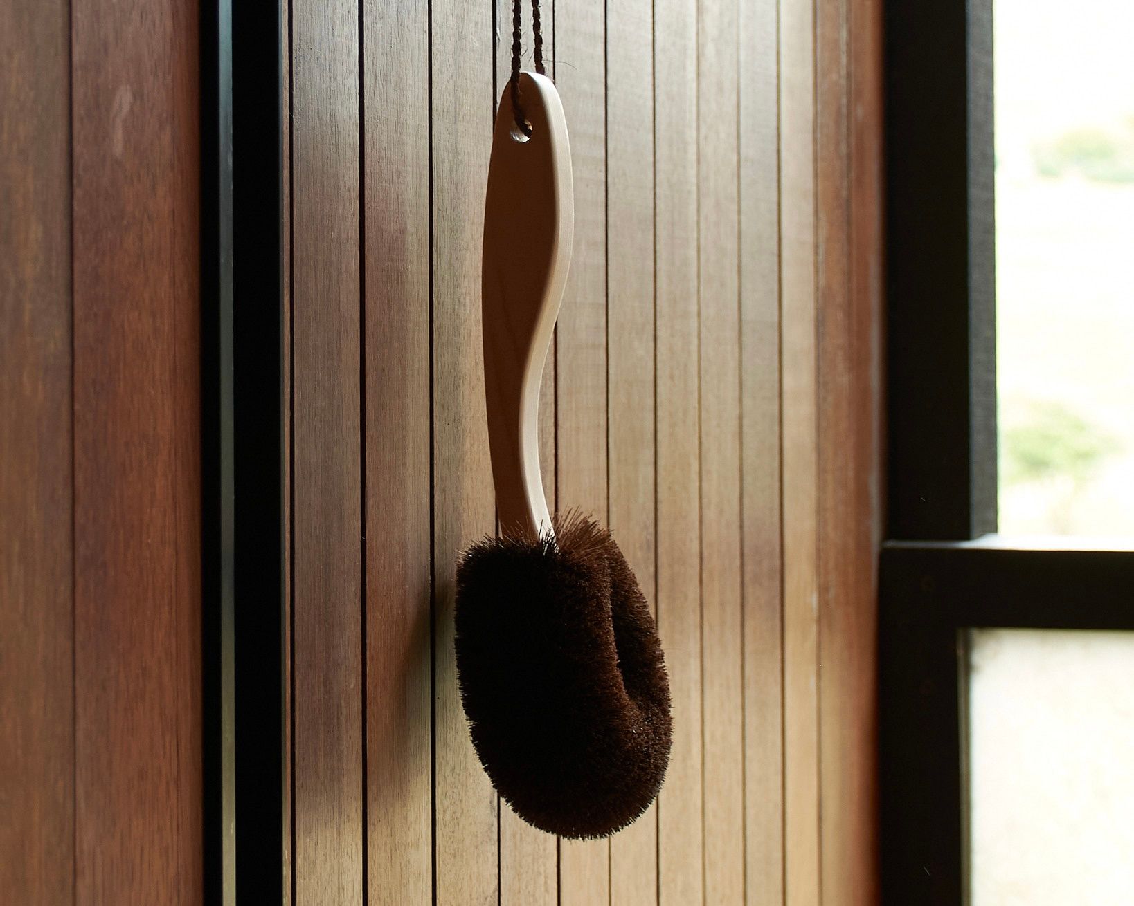 short handled wood and palm fibre body brush hanging in an outdoor shower