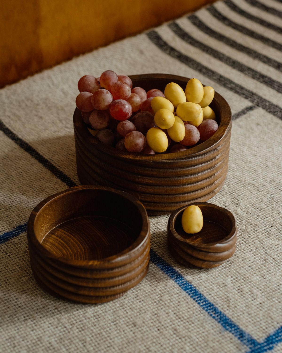 A collection of three Torsade hand turned bowls photographed on a woven blanket with a wooden background