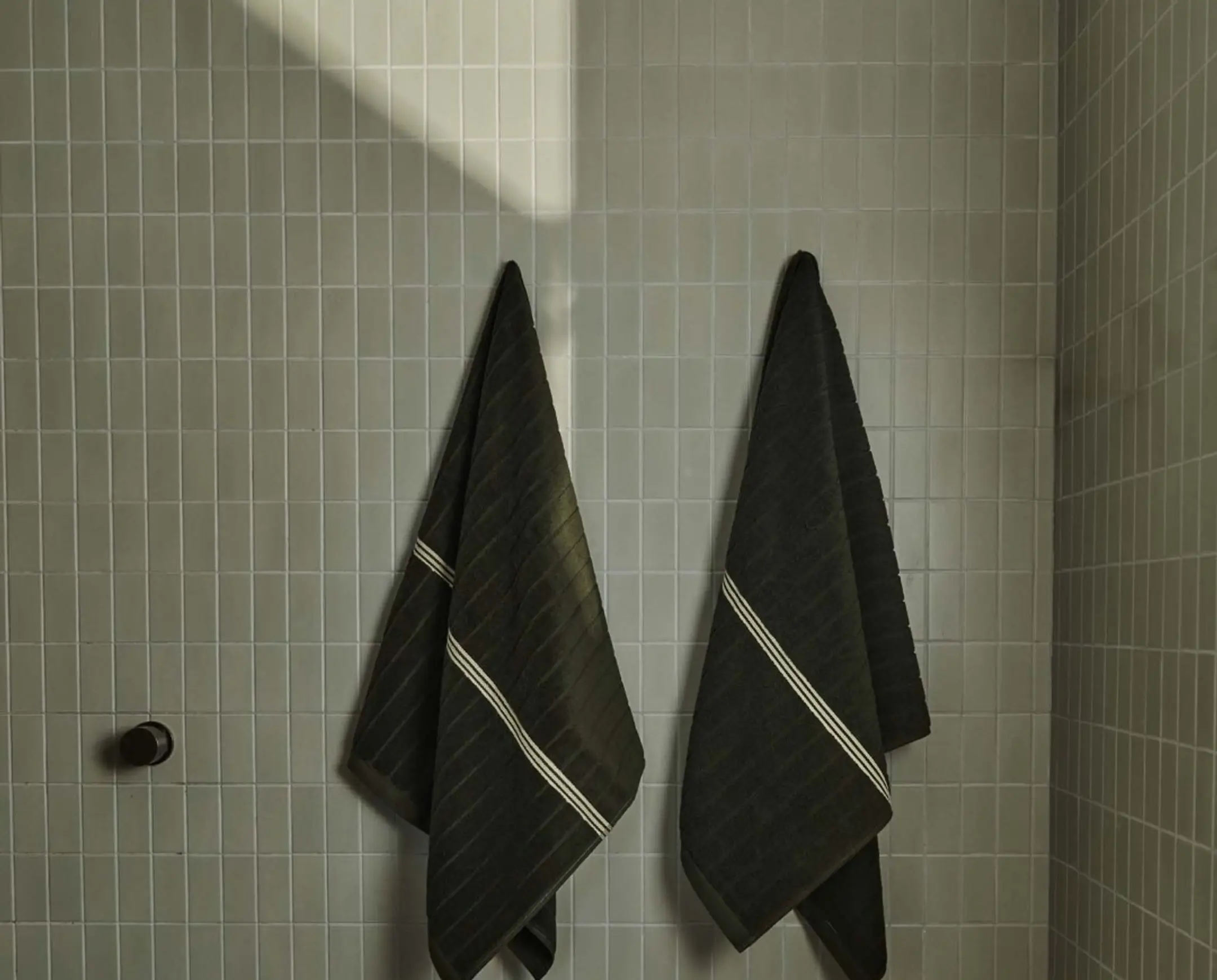 Two deep green bath towels hung up in a bathroom with pale green tiles