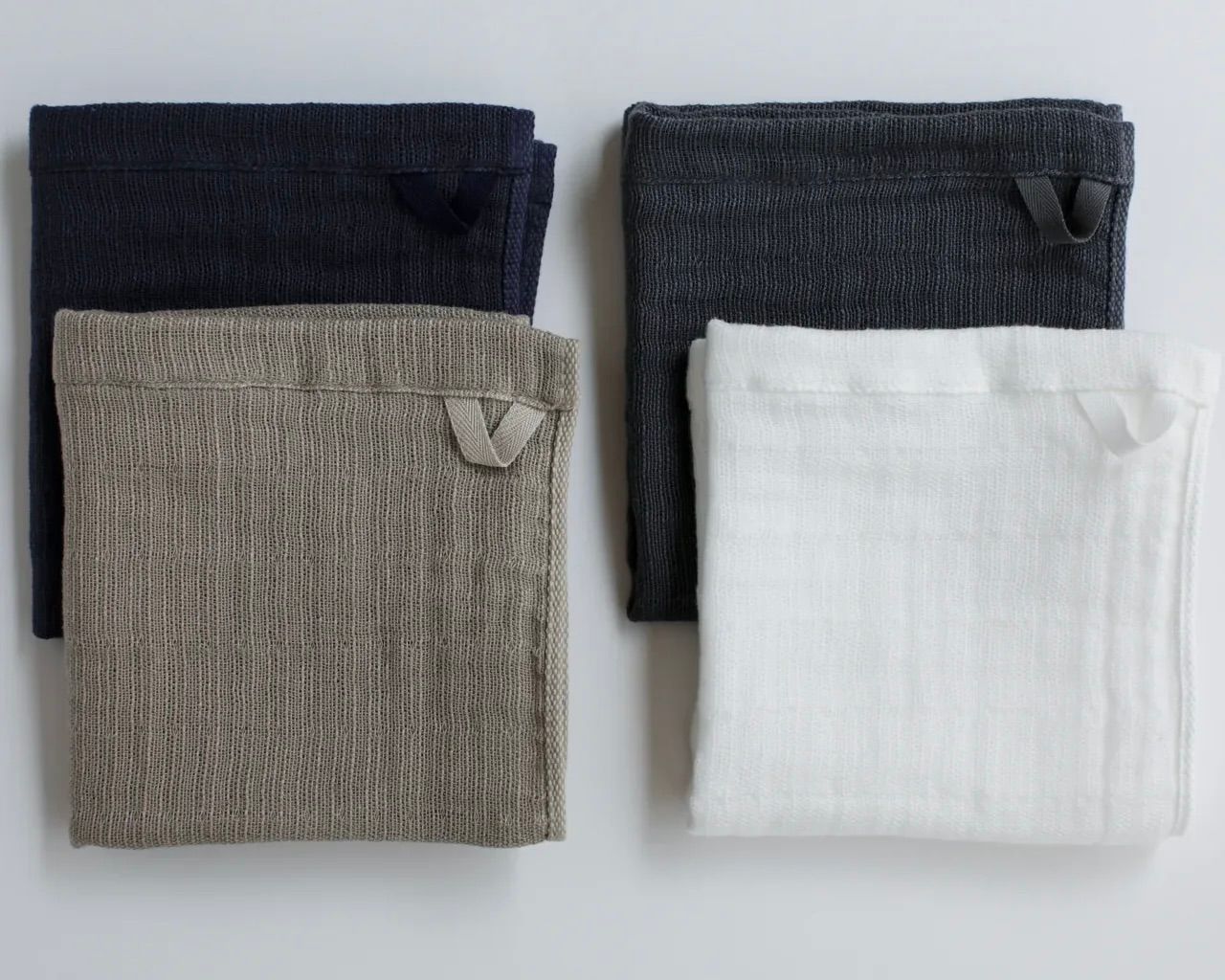 A collection of four folded Shinto 2.5 Ply Gauze washcloths on a white background, in charcoal, beige, white and navy.