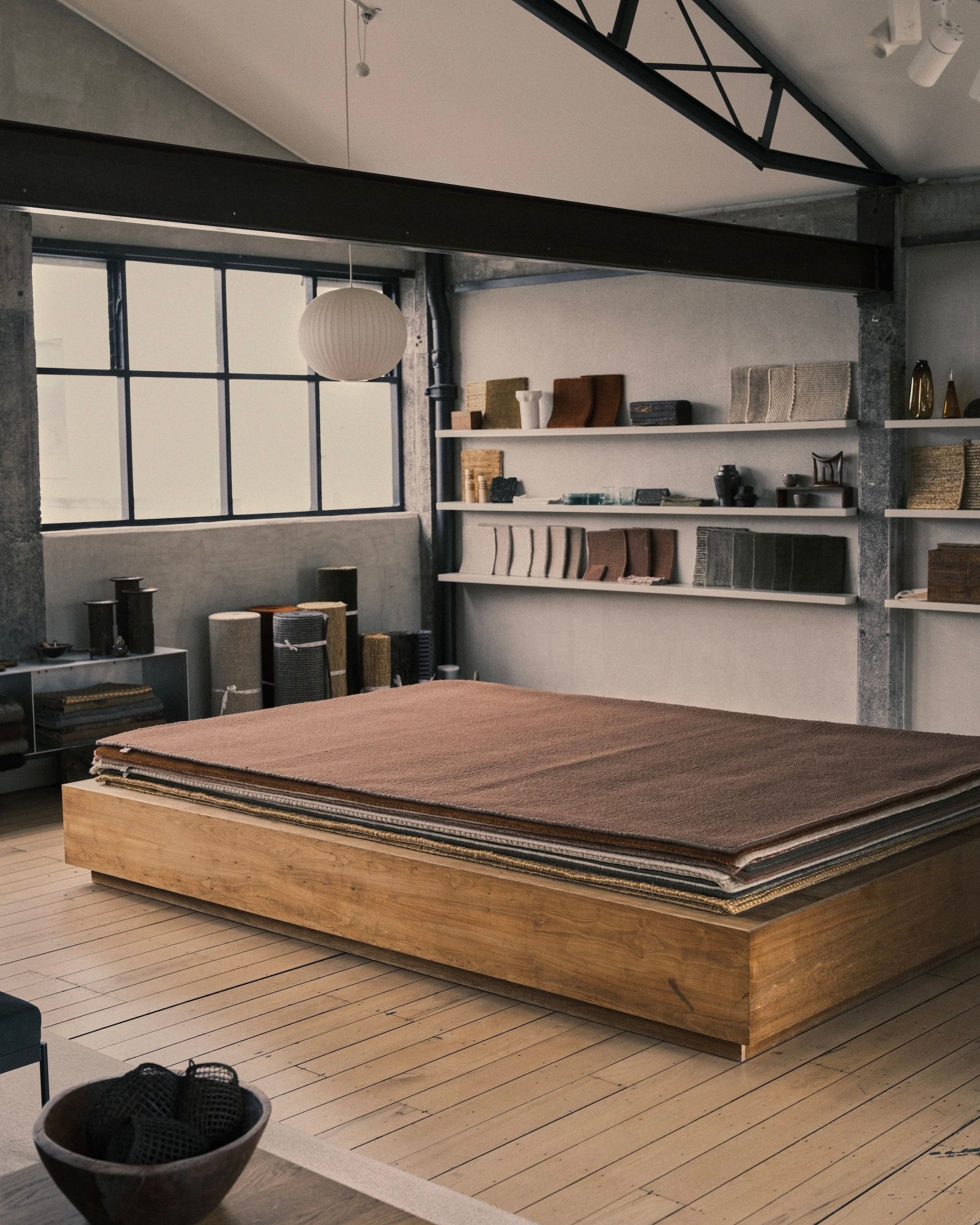 inside of Nodi's showroom with a stack of rugs and shelves with Handcrafted modern pieces and carpet swatches on them