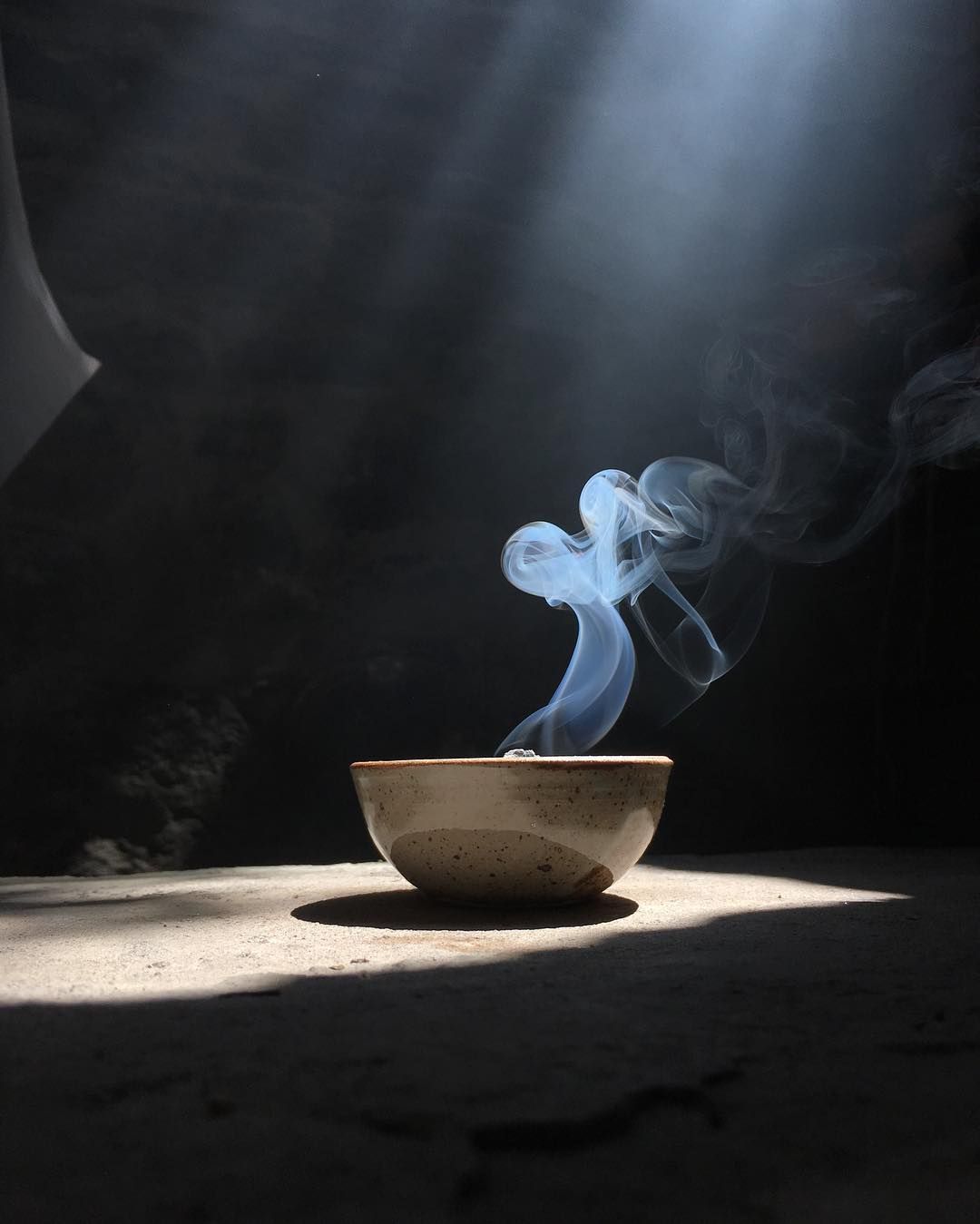 Palo Santo Incausa incense brick burning in a ceramic bowl on a table with a dark light shafted background and a smoke swirl
