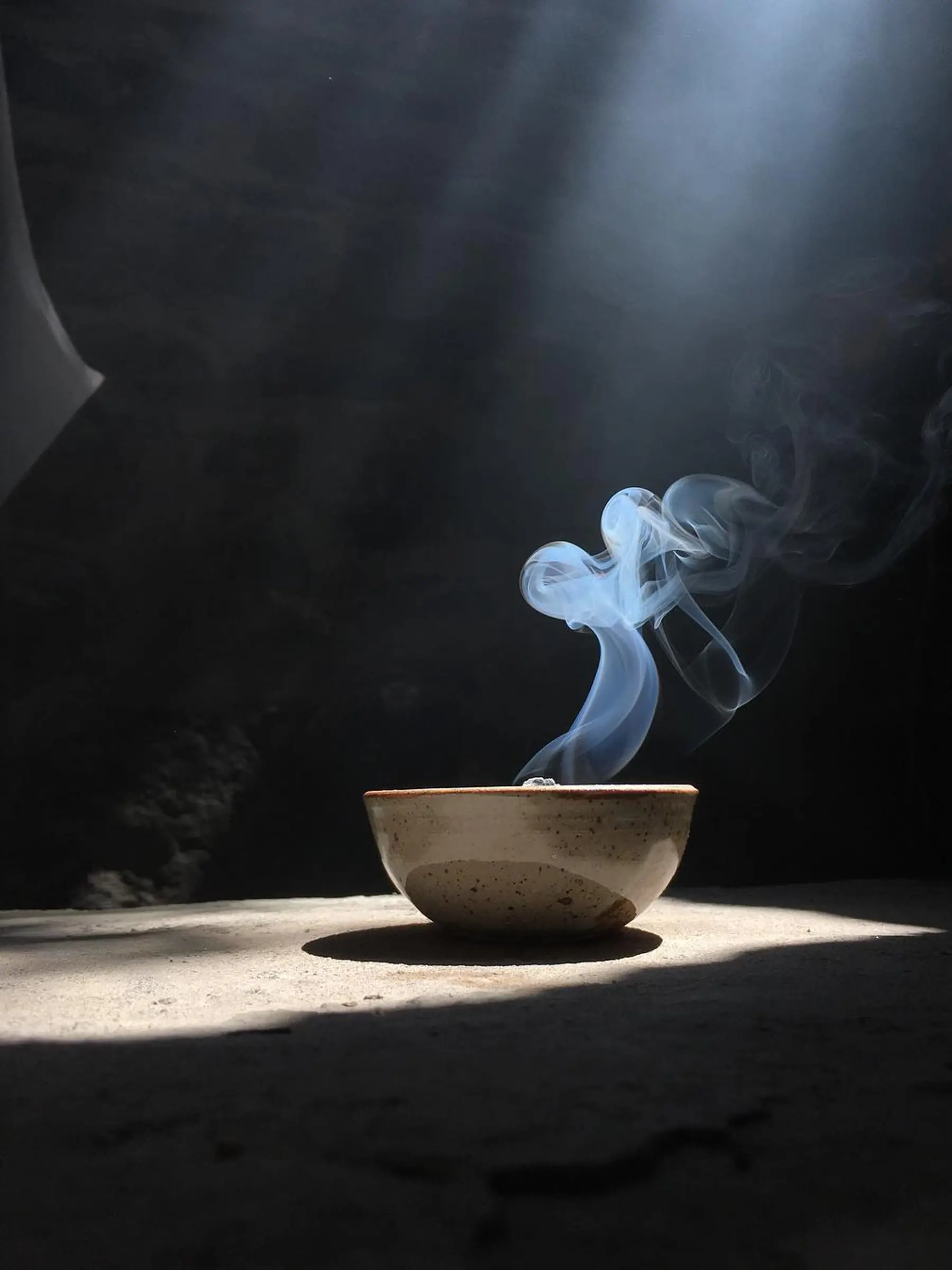 Palo Santo Incausa incense brick burning in a ceramic bowl on a table with a dark light shafted background and a smoke swirl