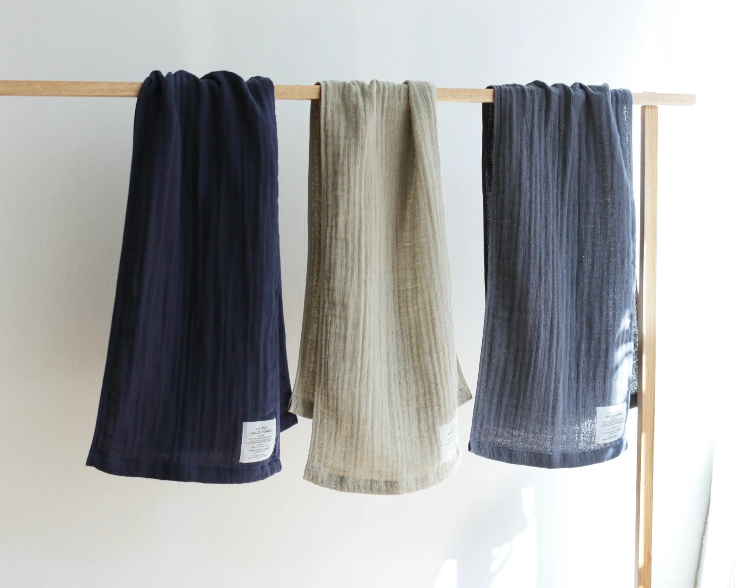 Three coloured Shinto bath towels hanging on a wooden rail in the sunshine