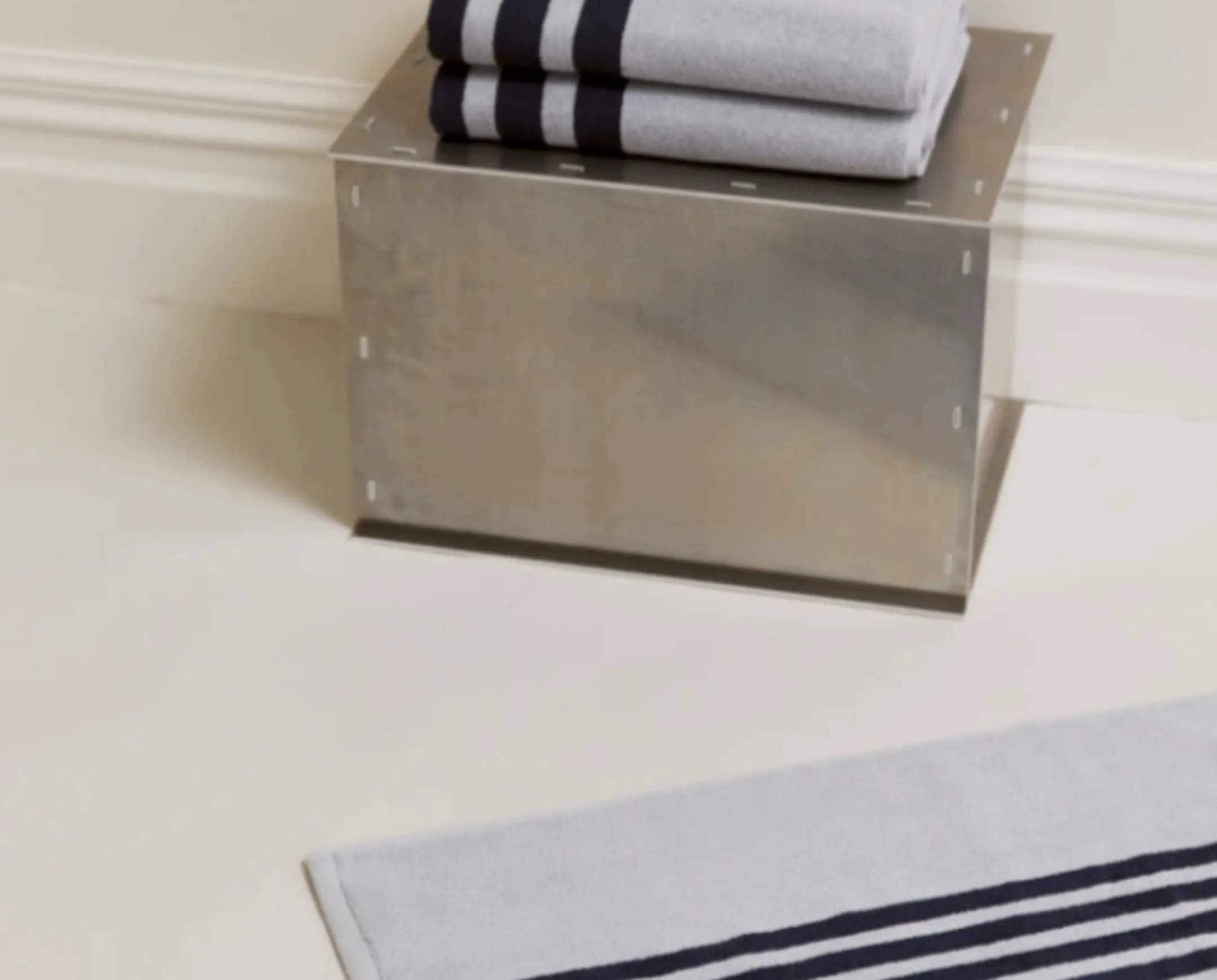 A pale blue bath mat on the floor next to a metal stool with towels onto