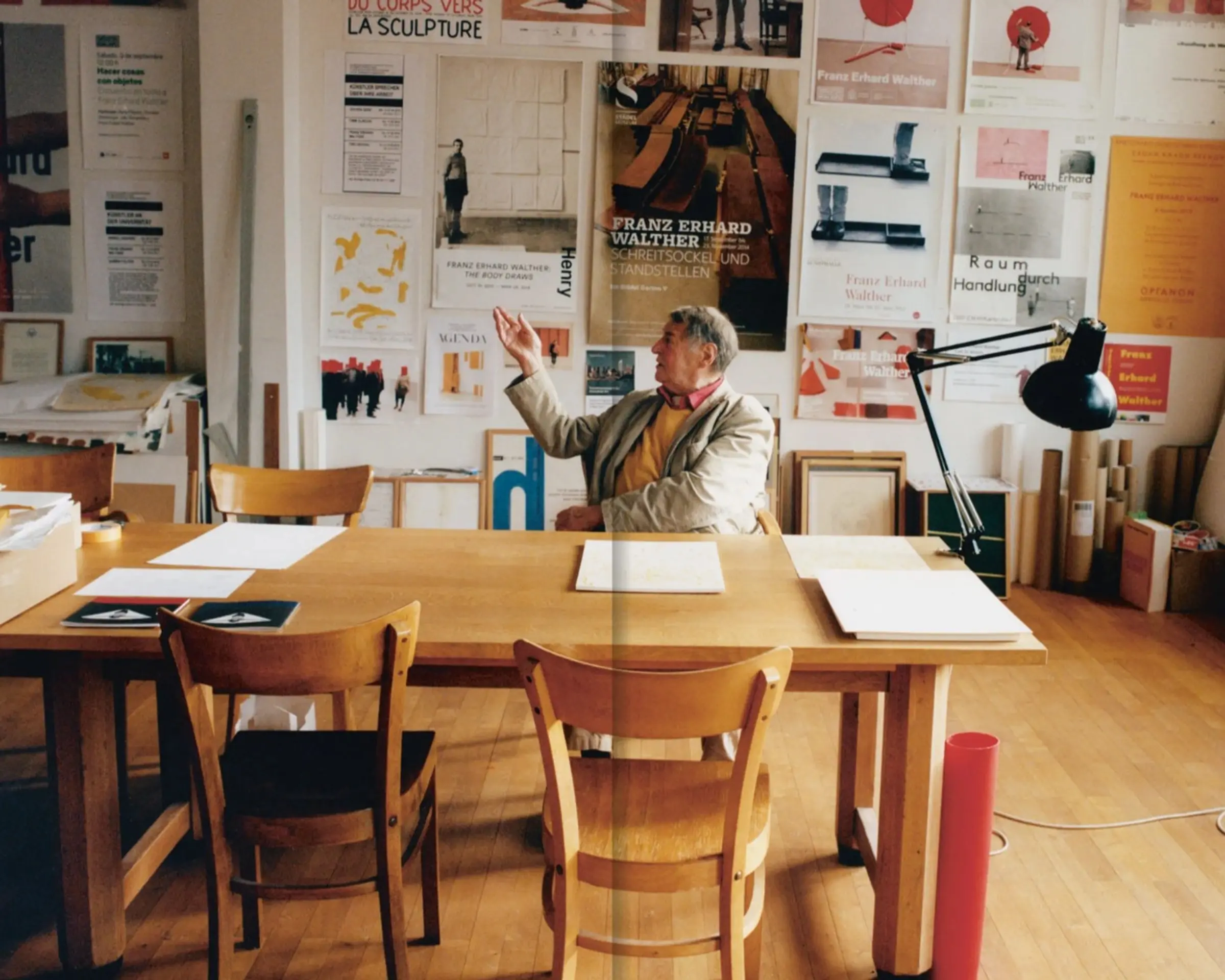 a photograph of a man sitting on a dining table with posters coving the walls