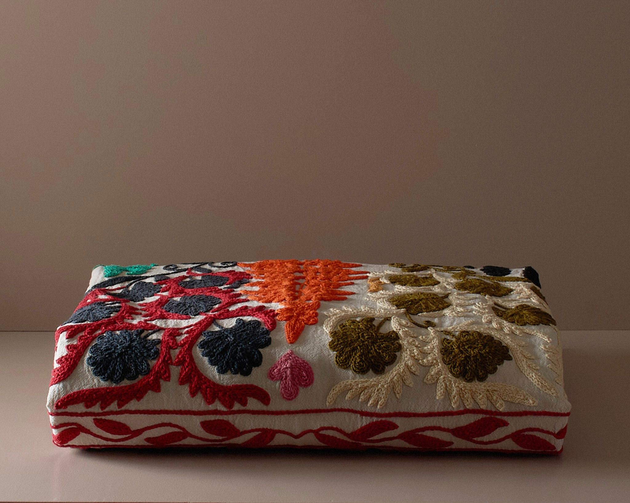 A multi colored embroidered suzani bedcover on a neutral colored plinth 
