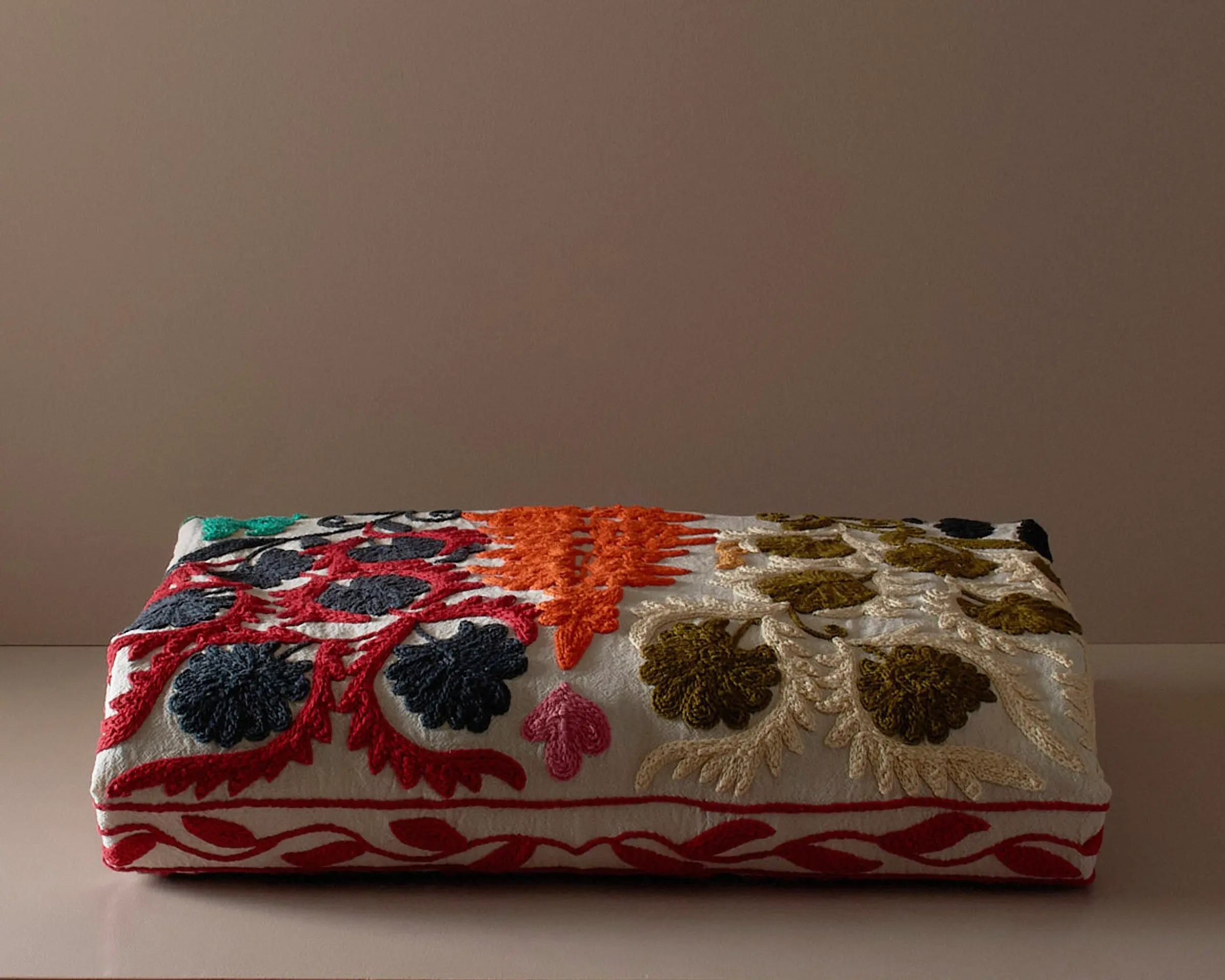 A multi colored embroidered suzani bedcover on a neutral colored plinth
