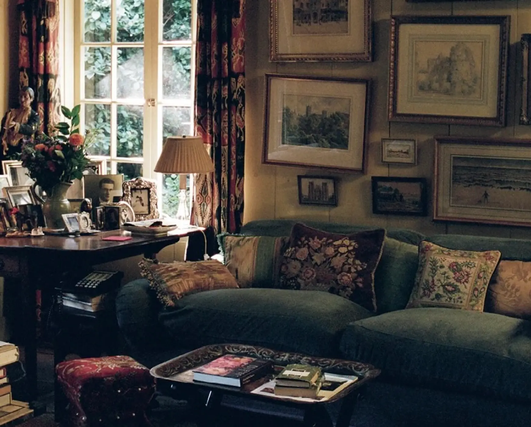 An image from Scenery magazine number 4, Inside of a living room filled with paintings on the wall, a blue couch with cross stitched cushions, decor covering the side tables and a vase of flowers