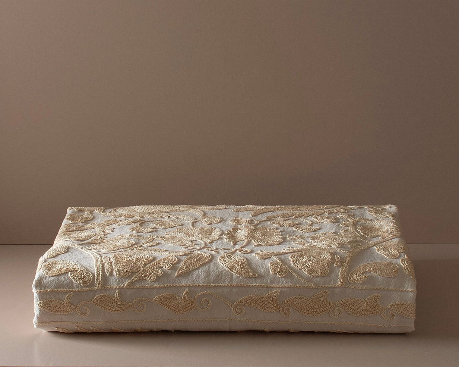 An embroidered suzani bedcover on a neutral colored plinth 