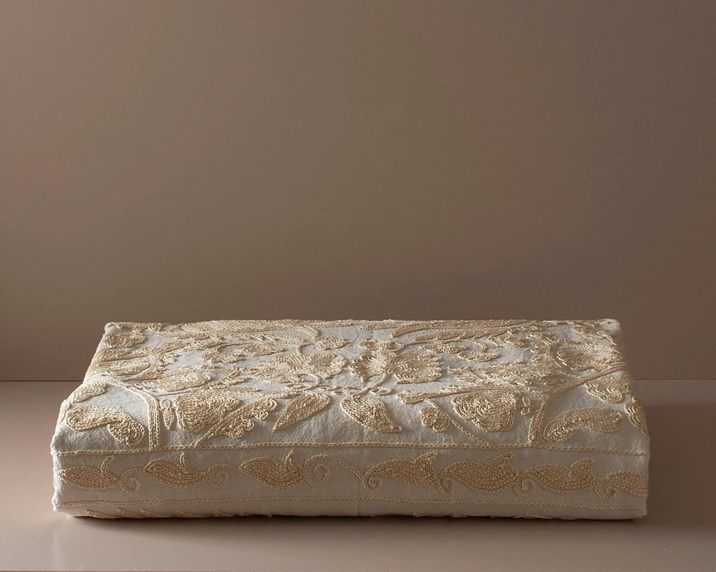 An embroidered suzani bedcover on a neutral colored plinth