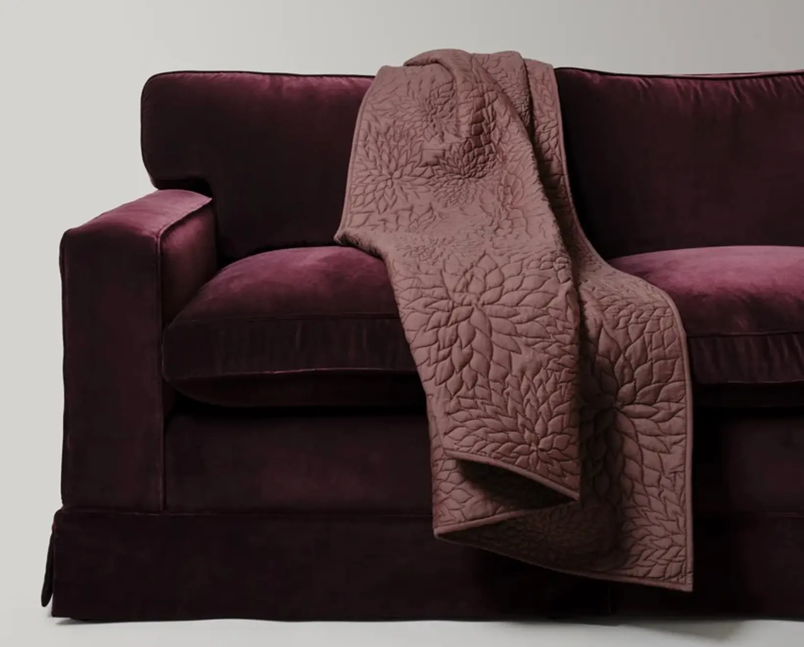 The Dhara Tuberous Throw by Studio Ford, woven from a silk-cotton blend and hand-dyed to a rich chocolate brown, subtle lustre that shifts beautifully with the light draped on a deep purple velvet sofa.