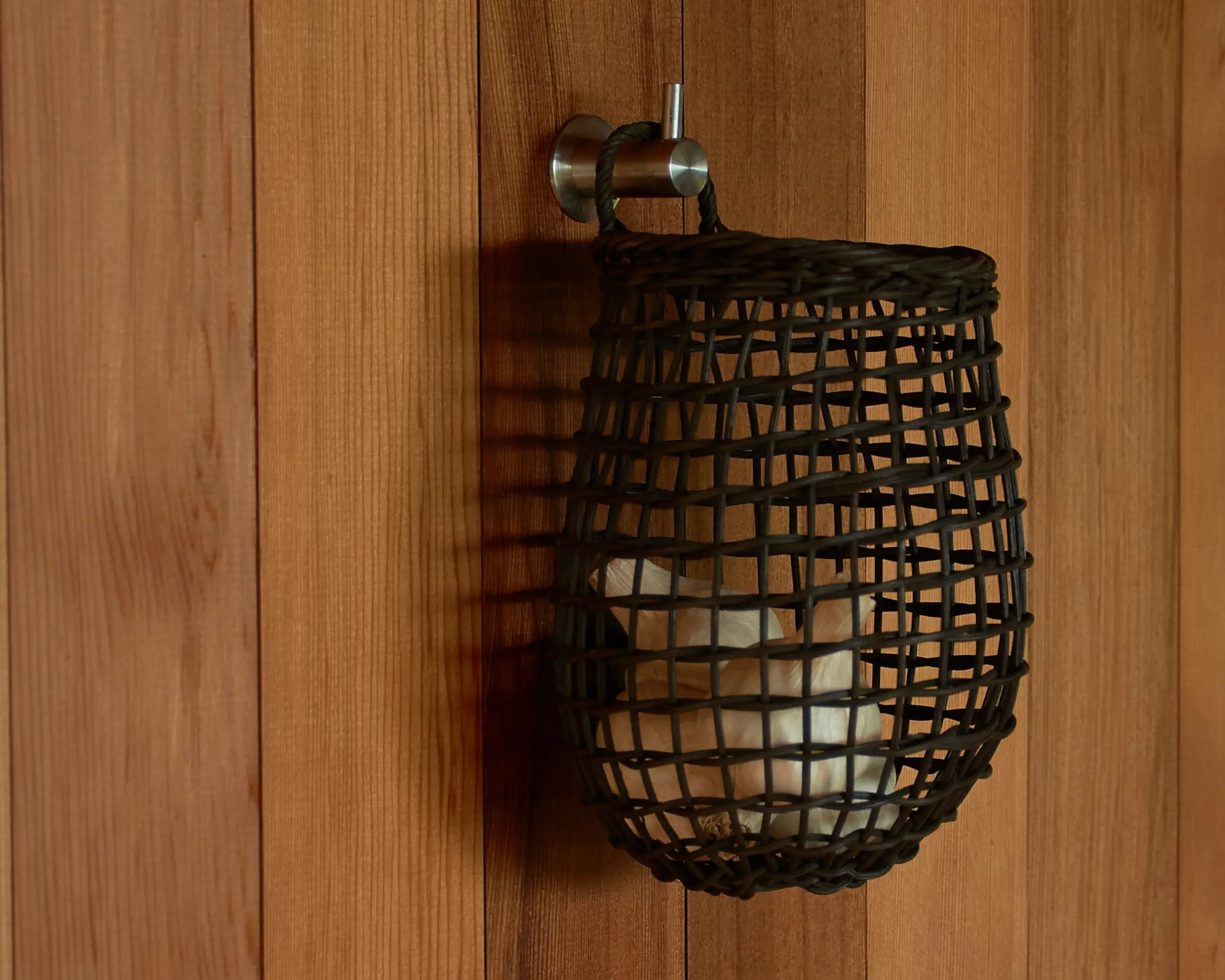 a rattan core woven garlic basket hanging on a wooden wall