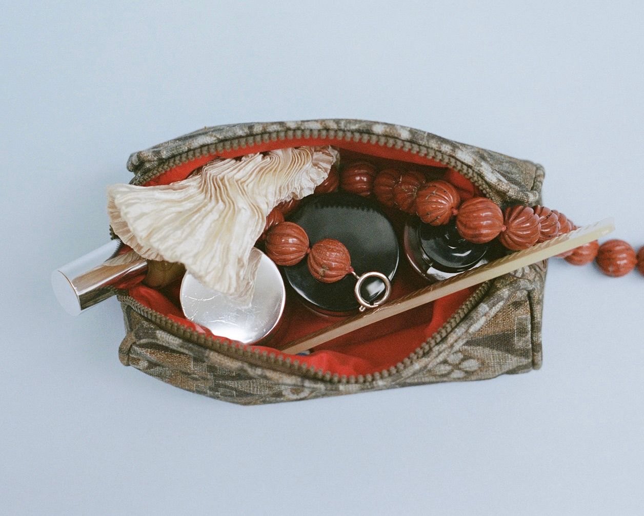 The Autumn Sonata Emilie toiletry bag in small with a string necklace, pots of lotion and lip products inside
