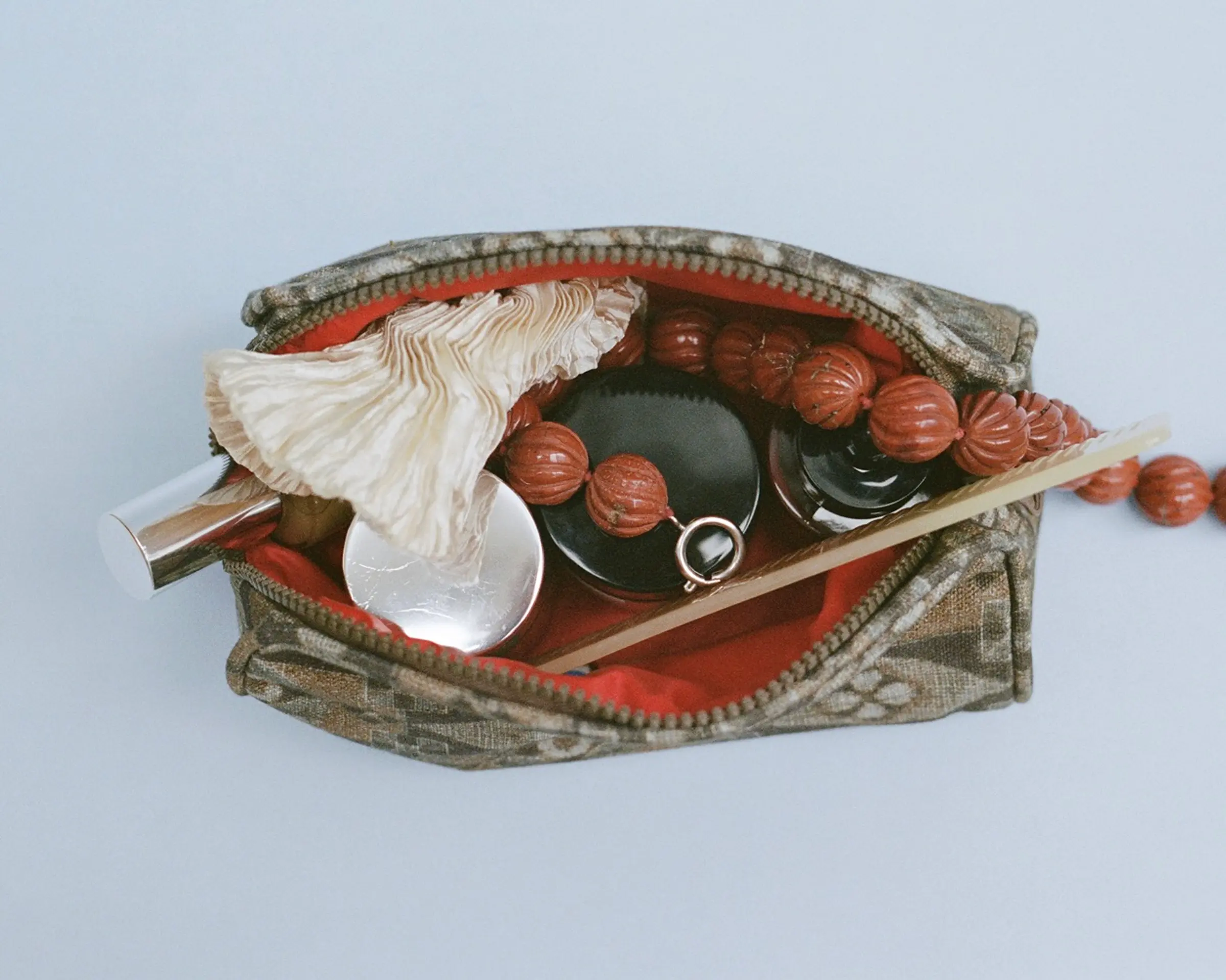 The Autumn Sonata Emilie toiletry bag in small with a string necklace, pots of lotion and lip products inside