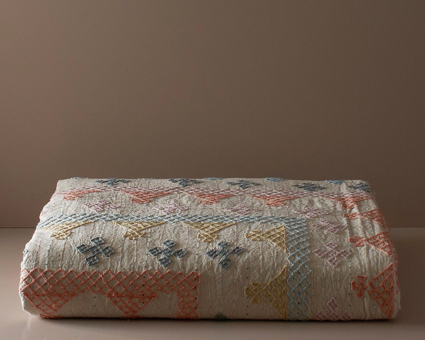 Queen Size Cross-stitch Cotton Kantha Bedcover on a neutral coloured plinth.