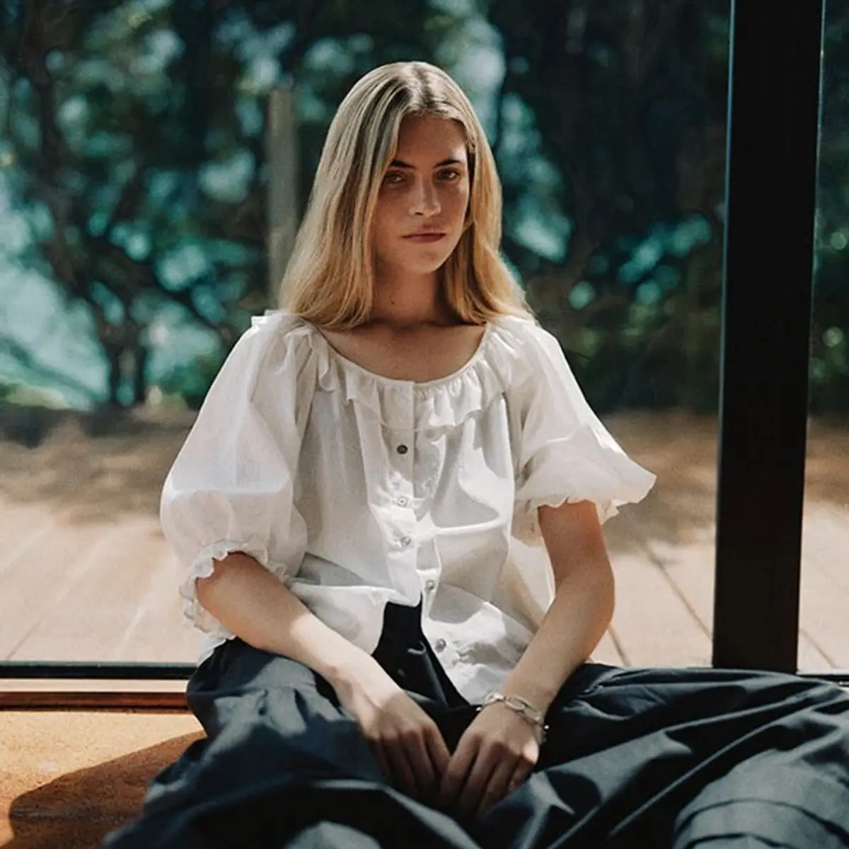 a model wearing a Mahsa cream ruffle blouse in a house leaning against black architectural glass joinery
