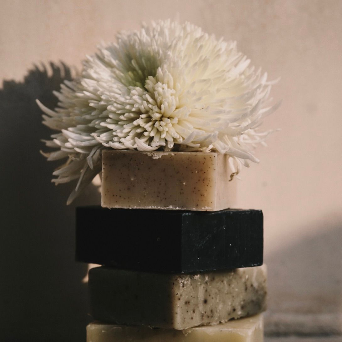 Handcrafted Tuétal cold process bar soaps stacked with white chrysanthemum flowers in soft natural light.