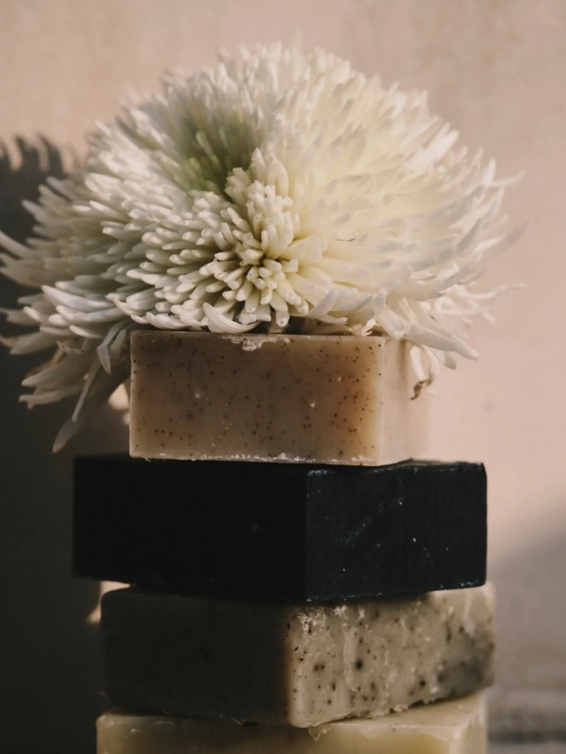 Handcrafted Tuétal cold process bar soaps stacked with white chrysanthemum flowers in soft natural light.