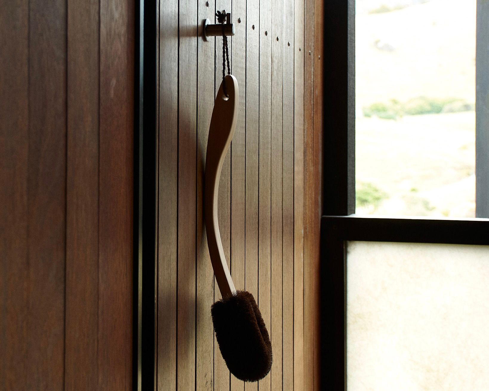 long handled body brush hanging in an outdoor shower 