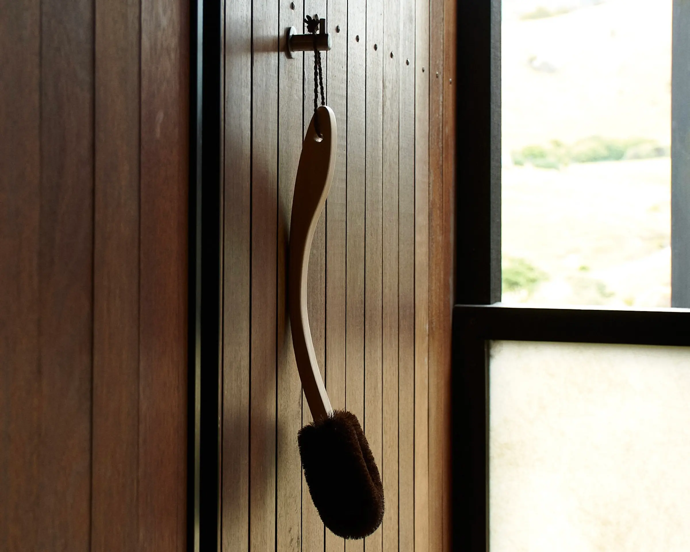long handled body brush hanging in an outdoor shower