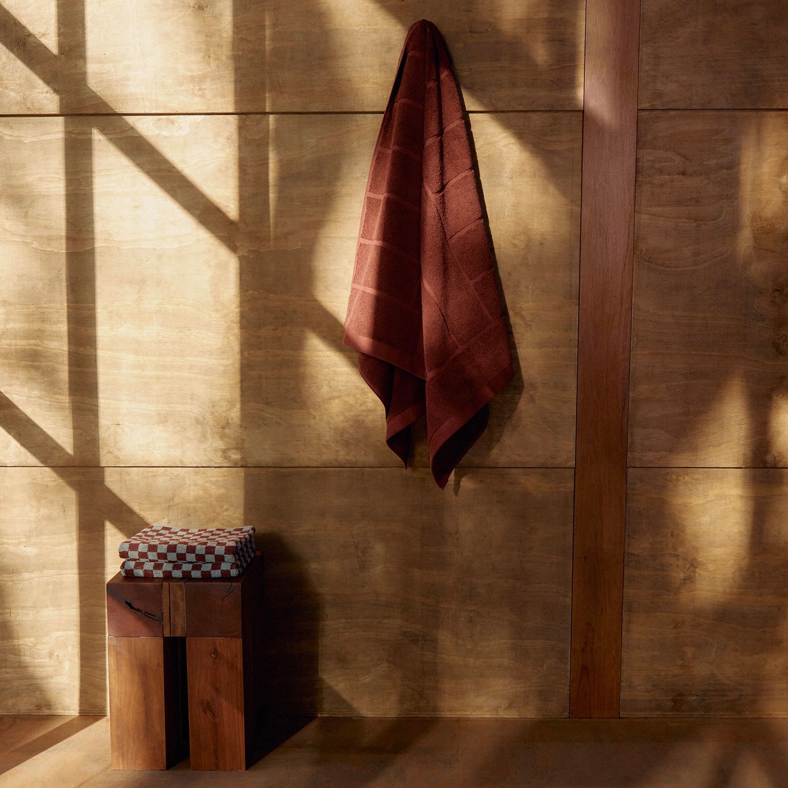 a towel hung on a wood wall with a small square stool next to it 