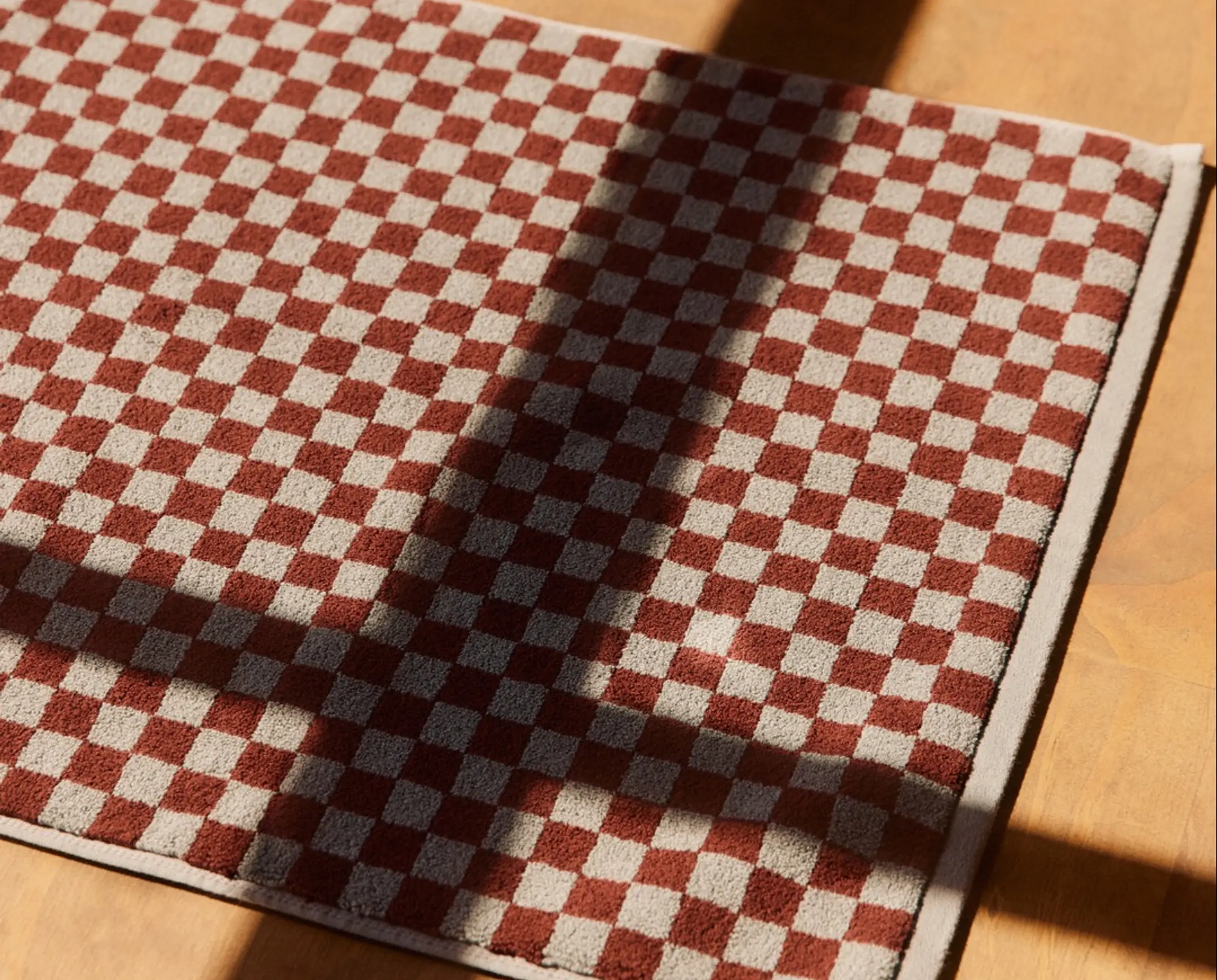Checkered bath mat on a wooden floor with shadows from the windows lines coming through